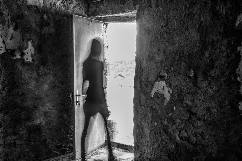 A shadowy, ghost-like figure steps through a doorway into blinding light, its form blurred as if vanishing. This image represents the haunting moment from 'A Waitress’s Final Encounter with Candle Face.'