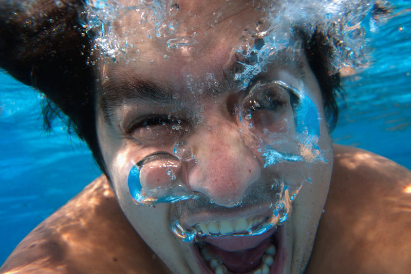 An underwater close-up of a Candle Face victim, his eyes squeezed shut and mouth open as bubbles escape. The distorted expression conveys both struggle and final moments beneath the surface. Related to Candle Face Chronicles.