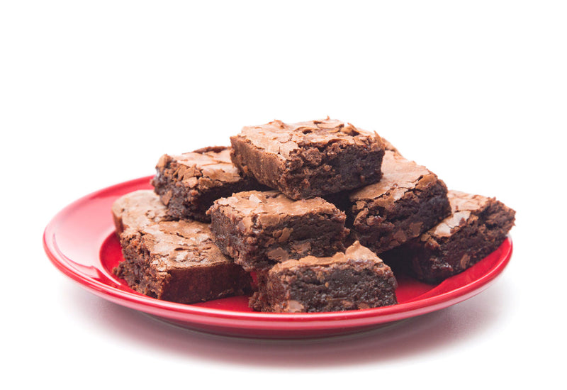 A stack of rich, fudgy brownies with a cracked top sits on a red plate against a white background. Image titled 'Struggles Beneath the Bridge.'
