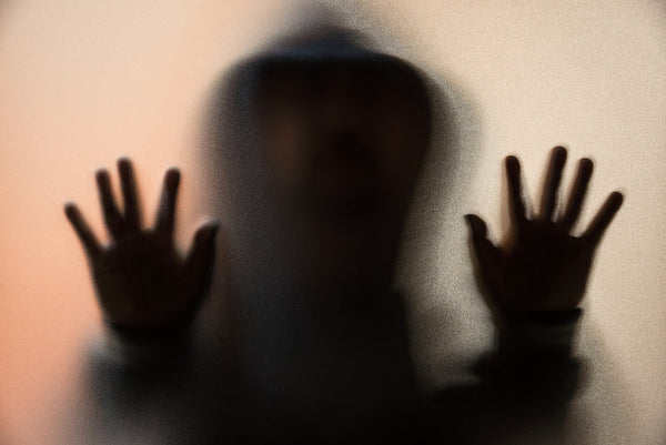 A blurred figure with hands pressed against a frosted glass, creating a ghostly and distorted appearance. The soft, hazy lighting adds a disturbing effect. This image, titled 'An Unclear Vision of Figures in the Crystal Ball,' symbolizes the mysterious an