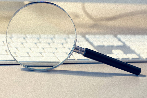 A magnifying glass resting on a white keyboard, suggesting a focused investigation or search. The title 'Candle Face Chronicles: Searching for the Man Behind the Drumbeat' implies an ongoing investigation within the Candle Face Chronicles series by Branch