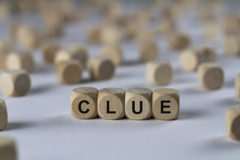 Wooden blocks spelling "CLUE" are placed on a white surface, surrounded by scattered blank wooden cubes. The image represents the concept of foreshadowing and hidden hints in storytelling.