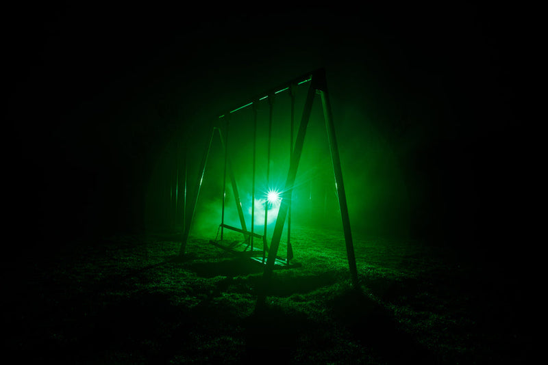 A dimly lit swing set glowing in green mist—the scene where a young child is taken by Candle Face, as recounted in Candle Face Chronicles: 'Mama’s Last Embrace.'