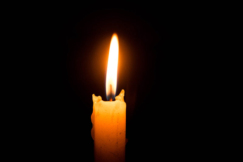 A single candle burns against a pitch-black background, its flame flickering with quiet intensity. This image represents 'My Last Wish,' symbolizing a final plea, remembrance, and the fragile line between light and darkness in the presence of Candle Face.