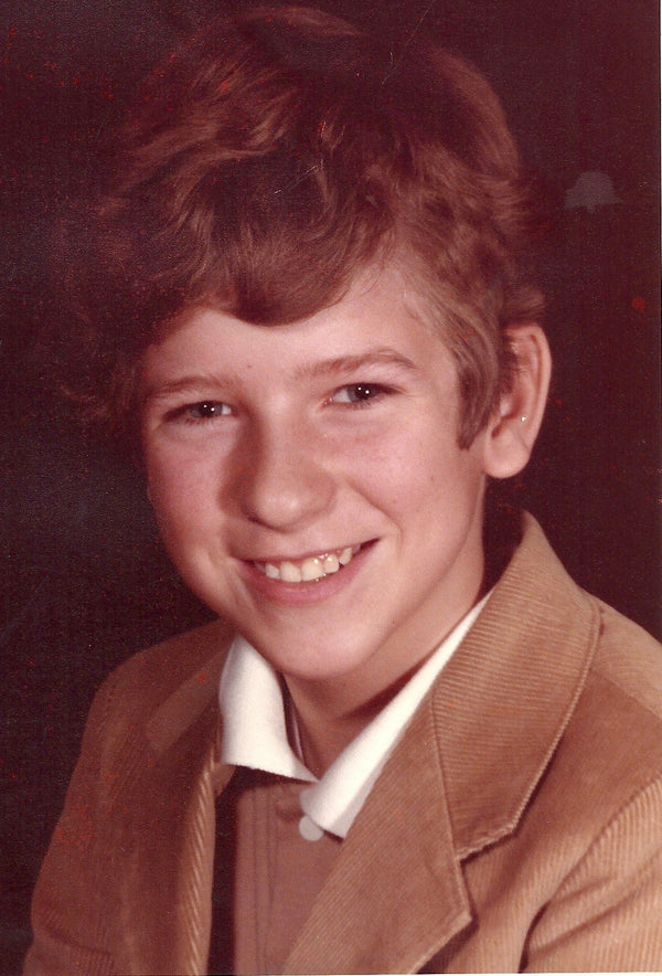 Ray Mills, a young boy with wavy light brown hair and a warm smile, dressed in a tan blazer over a white collared shirt. Image titled 'Ray Mills  - The Empty Lot Next Door.'