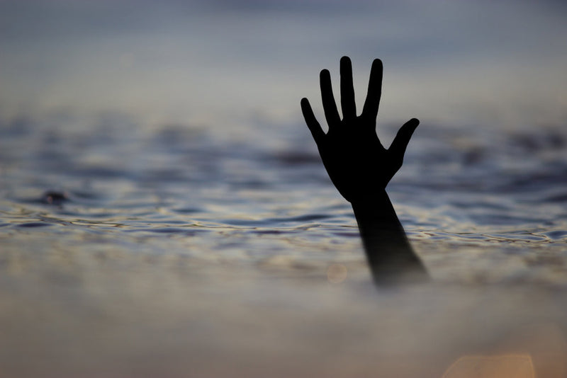 Silhouette of a hand reaching above the water’s surface at sunset, symbolizing the victims of Lady Bird Lake and the legend of Isabel, the forgotten daughter of La Llorona, said to pull people under.