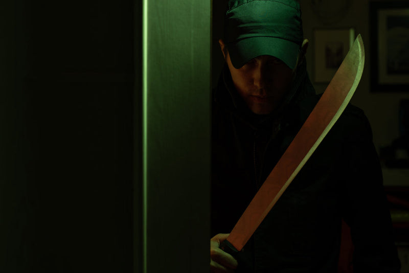 A shadowed figure in a cap grips a machete, bathed in green light—an image from Candle Face Chronicles, featured in the journal entry 'Candle Face Victim #3: Laughter to Terror - A Night Gone Bad.'