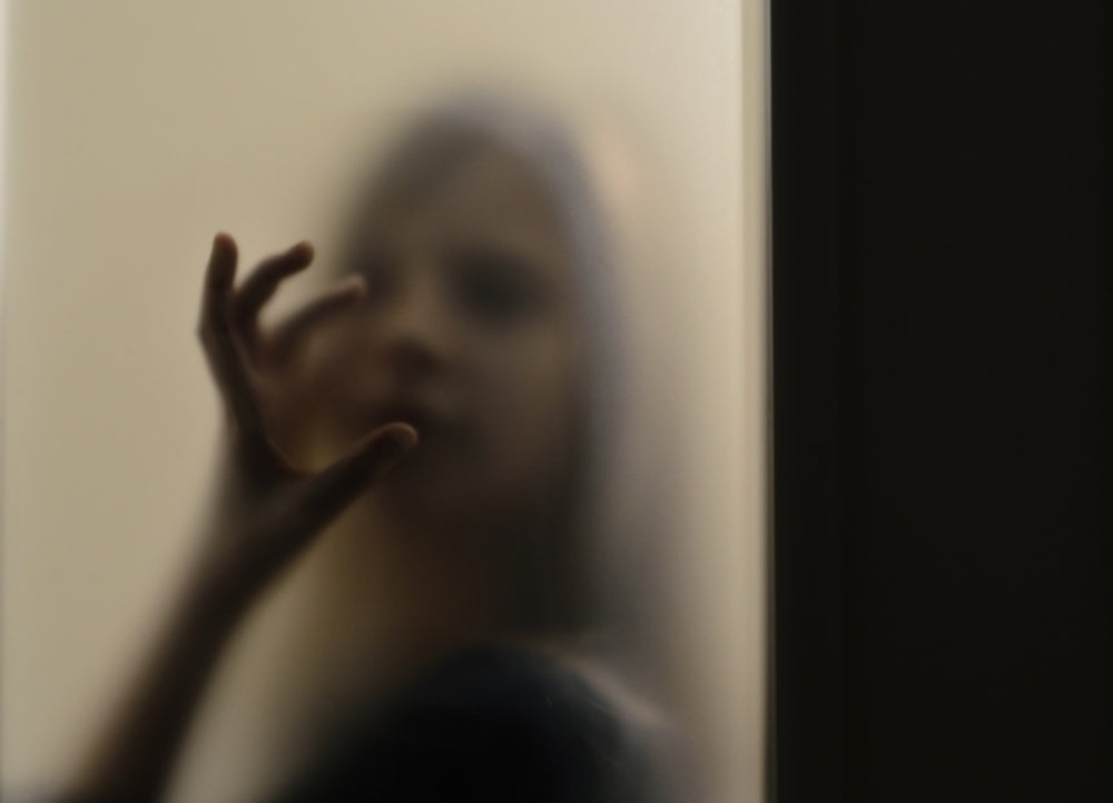 Faint silhouette of a girl reaching through frosted glass—one of the Remembered souls sealed inside the scrolls, still pressing against the veil, longing to be seen, heard, and held in memory.