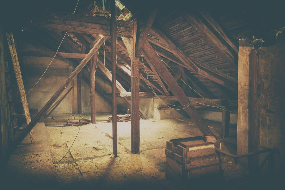 A dusty, dim attic space with exposed wooden beams and scattered boxes. Weathered parchment scrolls lie among old belongings, evoking a mysterious, long-forgotten storage area where Mr. Smoe kept the Scrolls of Souls.